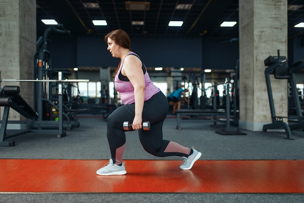 Übergewichtige Frau, die im Fitnessstudio mit Hanteln trainiert, aktives Training