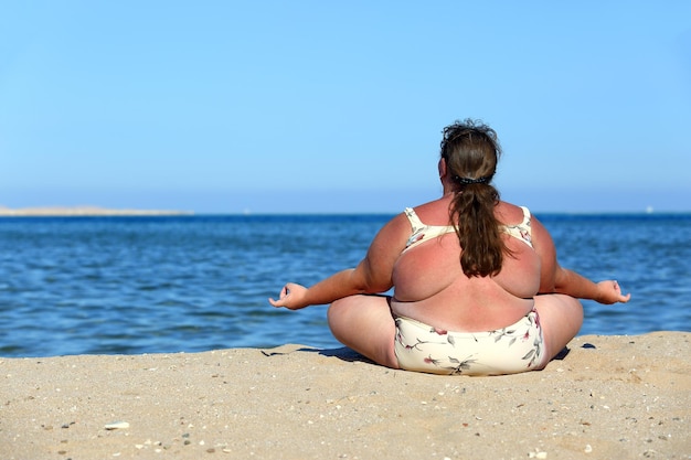 Übergewichtige Frauenmeditation am Strand