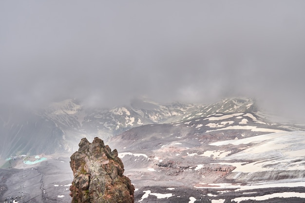 Berghänge und schwarzes Vulkangestein mit Schnee bedeckt. niedrige Wolken über den zerfurchten Gipfeln. Elbrus