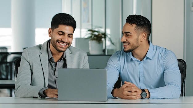 Überglücklich lächelnde männliche Mitarbeiter, die auf den Laptop-Bildschirm schauen, begeistert von unglaublich guten Nachrichten Fröhliche Mitarbeiter, die den Erhalt einer angezogenen Investitionsbenachrichtigung feiern Fröhliche Zusammenarbeit im Büro