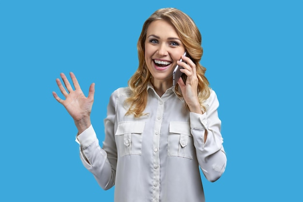 Überglückliche junge Frau, die am Handy vor blauem Hintergrund spricht