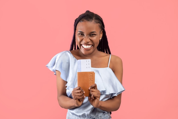 Überglückliche junge schwarze Frau mit Reisepass und Flugtickets, die in den Urlaub nach Übersee reisen
