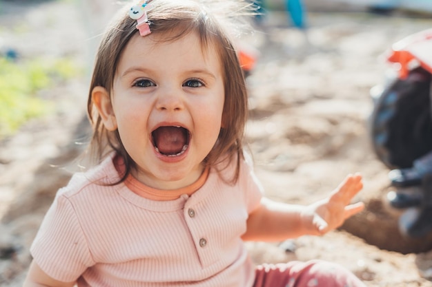 Überglückliches Babymädchen, das zu Hause im Hinterhof Sandkasten spielt Babyentwicklung Sommerferienspaß Gesunde Aktivität