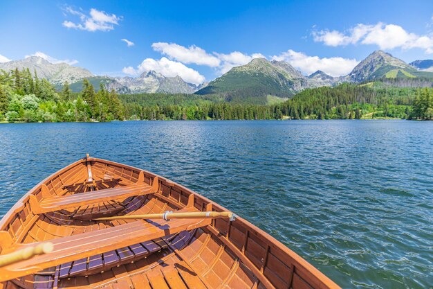 Bergsee mit Nadelwald, sonniger blauer Himmel des hölzernen Bootes, idyllischer Freiheitsreisehintergrund.