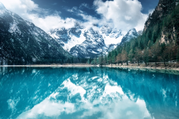 Bergsee mit perfekter Reflexion am sonnigen Tag im Herbst. Dolomiten, Italien. Schöne Landschaft mit azurblauem Wasser, Bäumen, schneebedeckten Bergen in den Wolken, blauem Himmel im Herbst.