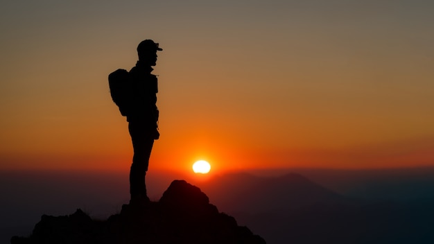 Bergsteiger auf dem Gipfel des Berges, der den fantastischen Sonnenuntergang beobachtet. In Silhouetten