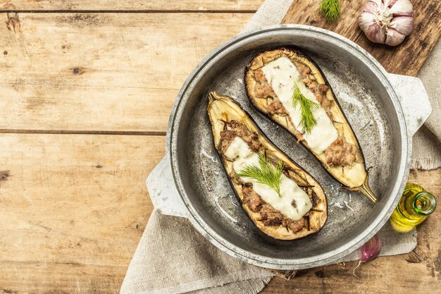 Berinjela recheada pronta para comer com carne moída, vegetais e especiarias. Fundo de madeira, utensílio de cozinha, estilo rústico, vista de cima