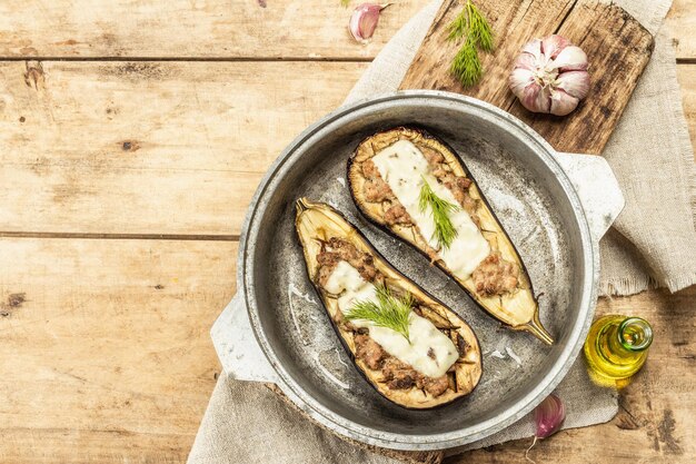 Berinjela recheada pronta para comer com carne moída, vegetais e especiarias. Fundo de madeira, utensílio de cozinha, estilo rústico, vista de cima