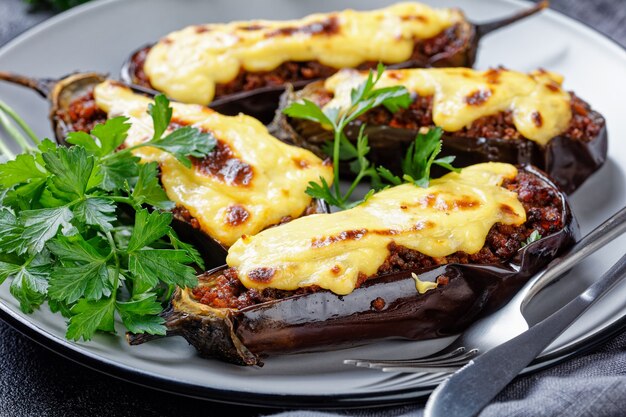 Berinjelas recheadas gregas com carne moída, tomates, cobertas com molho bechamel com queijo, servidas em um prato com salsa na superfície de concreto escuro, vista de cima, close-up