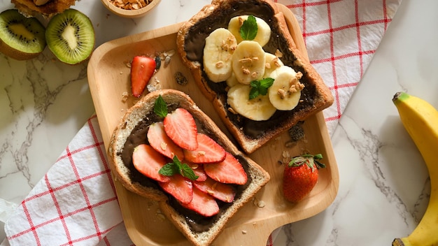 Überkopfaufnahme eines gesunden Toasts mit frischen Früchten mit hausgemachter dunkler Schokoladenaufstrich auf einer Holzplatte