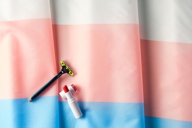 Überkopfaufnahme von Lippenstift und Rasiermesser auf einer Transgender-Flagge