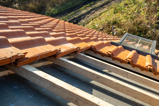 Überlappende Reihen von gelben keramischen Dachziegeln, die auf Holzbrettern montiert sind, die das Dach des Wohngebäudes im Bau bedecken.