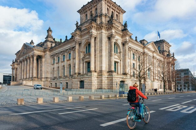 Berlim, Alemanha - 8 de dezembro de 2017: Senhora de bicicleta na arquitetura do edifício Reichstag com bandeiras alemãs em Berlim, capital da Alemanha no inverno na rua. Casa do parlamento alemão do Bundestag.