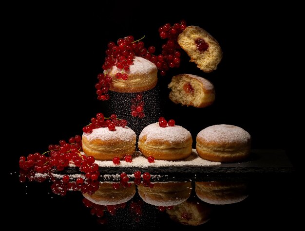 Berlinere donuts doces alemães polvilhados com açúcar de confeiteiro cheio de geléia de frutas cercado por frutas maduras em uma placa de ardósia preta em um fundo preto com reflexão