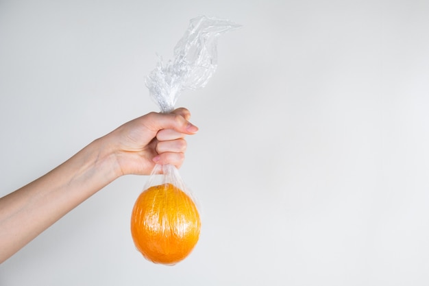 Übermäßiges Plastikgebrauchskonzept: Orange in der Plastikverpackung in einer Hand gehalten.