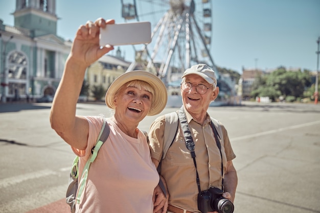 Übermütige grauhaarige Dame fotografiert sich und ihren Ehepartner vor dem Riesenrad in der Innenstadt