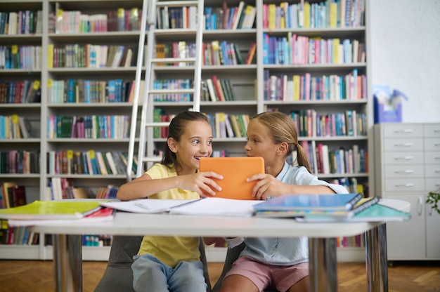 Übermütiges Schulmädchen und ihre nachdenkliche Mitschülerin in einer öffentlichen Bibliothek