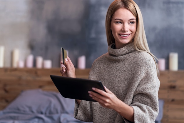 Überprüfen Sie Ihre Zahlungen. Hübsche junge entspannte Frau, die Tablette und Kreditkarte benutzt, während Rechnungen bezahlt und zu Hause bleibt.