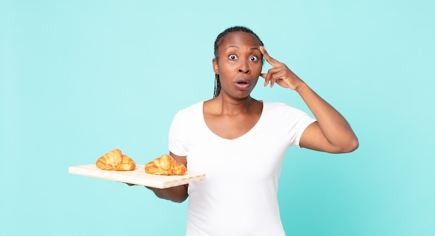 Überrascht aussehen, einen neuen Gedanken, eine neue Idee oder ein neues Konzept verwirklichen und ein Croissant-Tablett halten