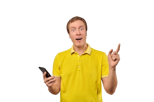 Überrascht junger Mann mit Smartphone isoliert auf weißem Hintergrund Lustige erstaunt Mann im gelben T-Shirt immer Push-Benachrichtigungen mit Smartphone Verblüfft glücklicher Kerl, der gute Nachrichten erhält