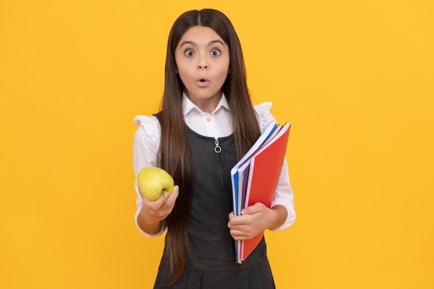 Überrascht Mädchen halten Apfel und Schulbücher gelber Hintergrund, Hausaufgaben.