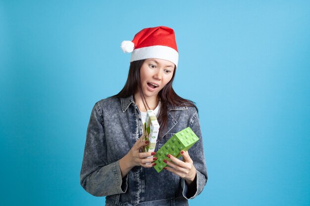 Überraschte asiatische Frau im Weihnachtsmannhut öffnet Neujahrsgeschenk