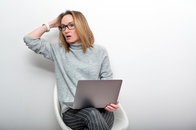 Überraschte blonde Frau mit Brille, die an einem Computer-Fernarbeitskonzept arbeitet, isoliert auf grau