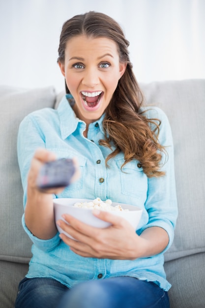 Überraschte Frau, die auf dem Sofa ändert Fernsehkanal sitzt