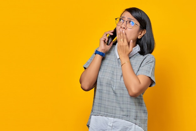 Überraschte junge Asiatin beim Empfang eines eingehenden Anrufs auf dem Mobiltelefon und Bedecken des Mundes mit der Hand