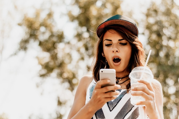 Überraschte junge Frau, die draußen intelligentes Telefon verwendet