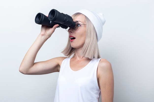 Überraschte junge Frau, die durch ein Fernglas auf hellem Hintergrund schaut.