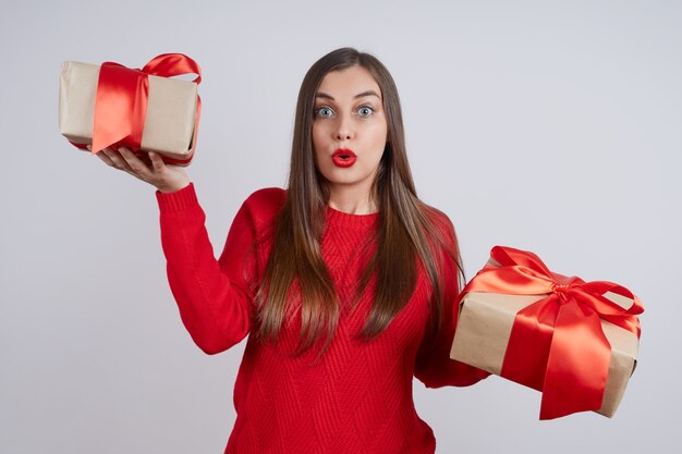 Überraschte junge Frau in einem roten Pullover, der Geschenkbox hält