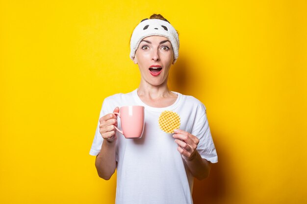 Überraschte junge Frau mit einer Tasse Kaffee und einer belgischen Waffel auf gelbem Grund