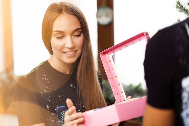 Überraschte junge Frau öffnet eine rosa Schachtel mit einem Geschenk