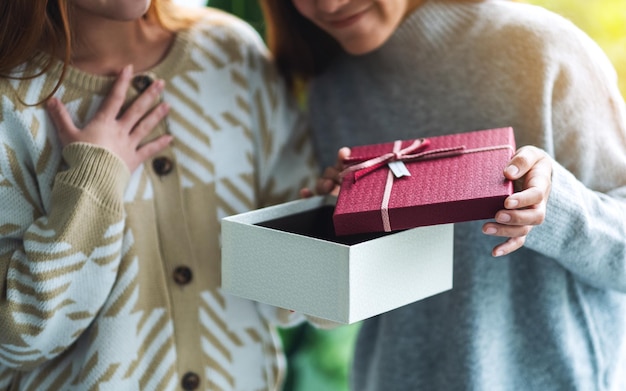 Überraschte junge Frauen, die zusammen eine Geschenkbox öffnen