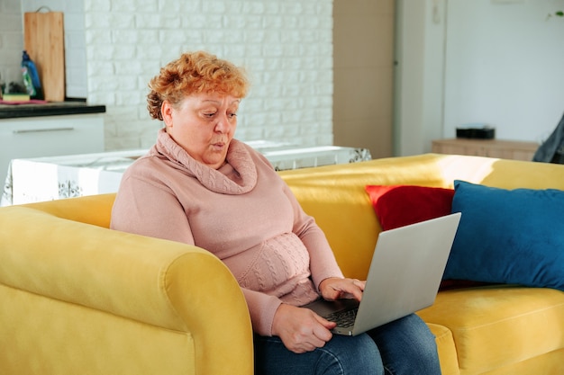 Überraschte kaukasische dicke Frau, die online auf dem Laptop schaut und eine schlechte Nachricht mit Internetverbindung sieht ...