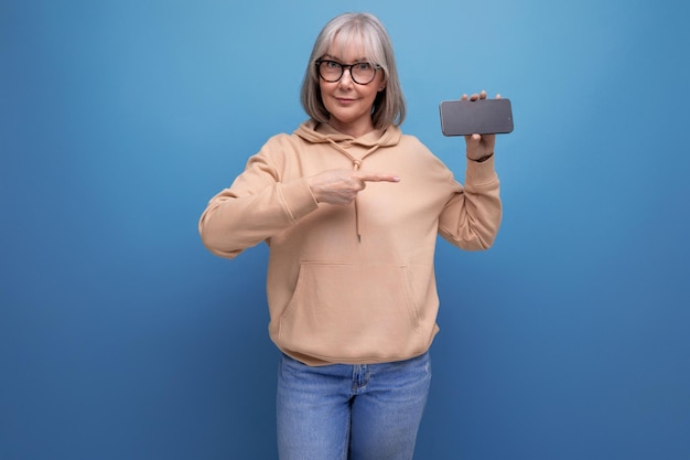 Überraschte reife Frau aus den 60ern mit grauen Haaren, die ihr Smartphone mit Mocap auf Studiohintergrund mit Kopierraum hält
