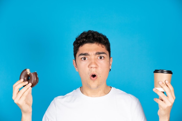 Überraschter hispanischer Teenager mit einer Einwegtasse Kaffee und einem Donut oder Donut