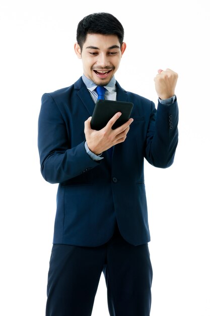 Überraschter junger asiatischer Geschäftsmann macht eine Ja-Geste beim Betrachten guter Nachrichten auf Tablet auf isoliertem weißem Hintergrund. Studioaufnahme, erfolgreiches Geschäftskonzept.