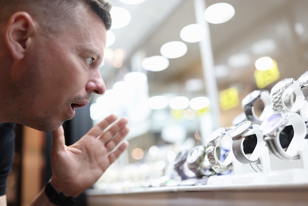 Überraschter Mann, der eine Glasvitrine mit teurer Uhr anschaut