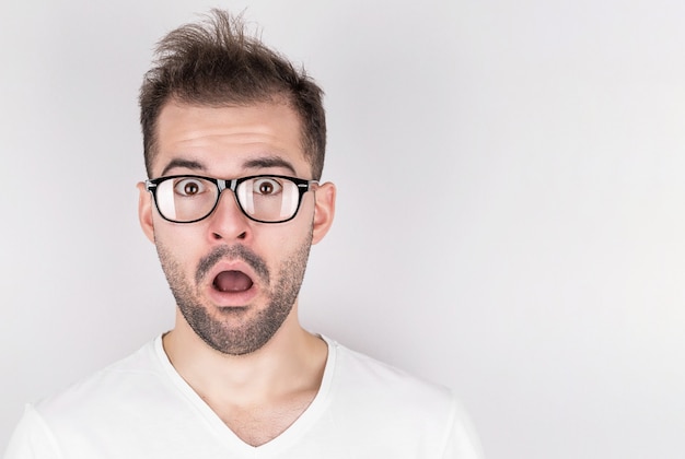 Überraschter Mann mit zerzausten Haaren, die Brille im weißen T-Shirt auf grauem Hintergrund tragen