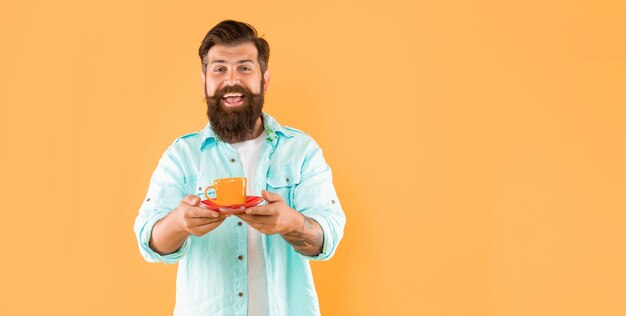 Überraschter reifer Hipster mit Bart, der Kaffeetasse auf gelbem Hintergrund mit Kopienraum hält Barista
