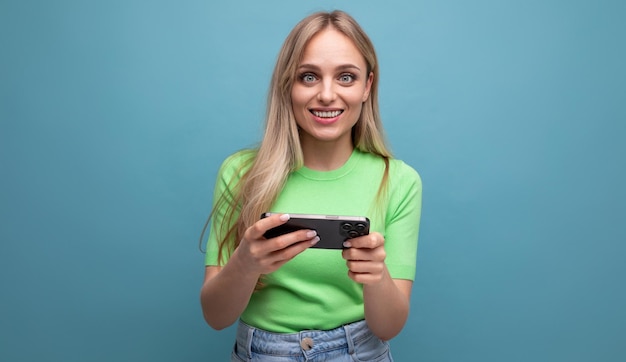 Überraschtes blondes Mädchen in lässiger Ausstattung, das ein Spiel am Telefon spielt und ein Gerät horizontal auf a hält