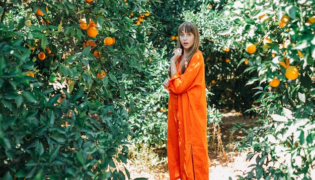 Überraschtes junges Mädchen in orangefarbenem Kleid posiert vor der Kamera im Orangengarten