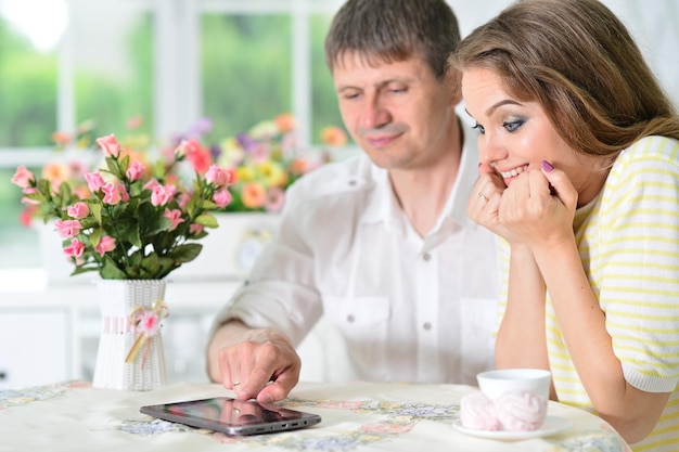Überraschtes junges Paar, das am Tisch sitzt und auf ein digitales Tablet blickt