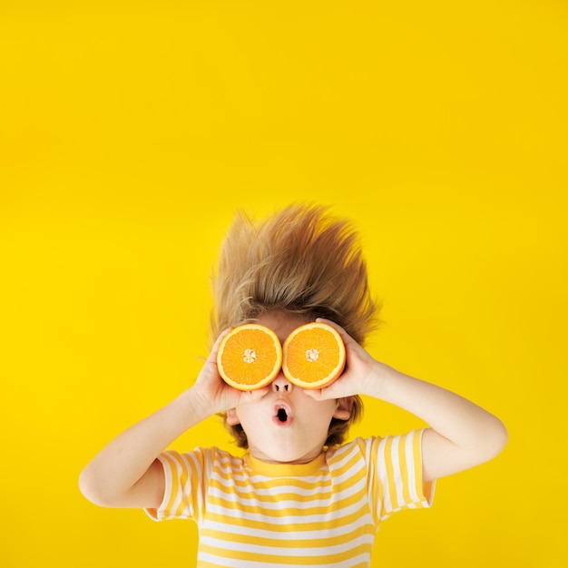 Überraschtes Kind, das Orangenscheiben wie eine Sonnenbrille hält