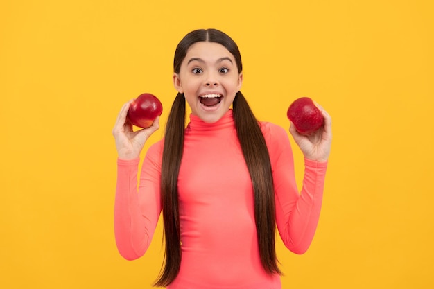 Überraschtes Kind mit rotem Apfel auf gelbem Hintergrund, der nährt
