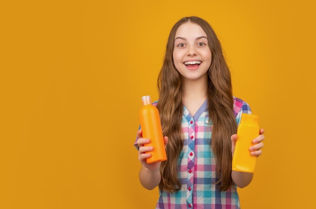 Überraschtes Kind mit Shampooflasche auf gelbem Hintergrund