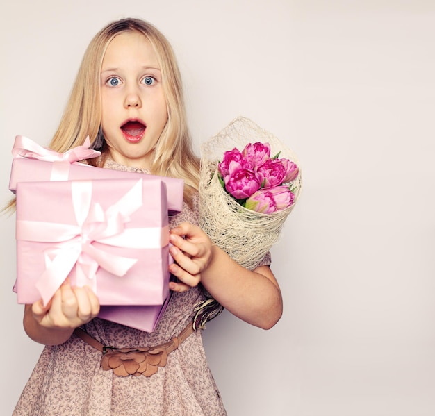 Überraschtes Kindermädchen mit rosa Blumen und Geschenkbox auf Hintergrund mit Kopienraum