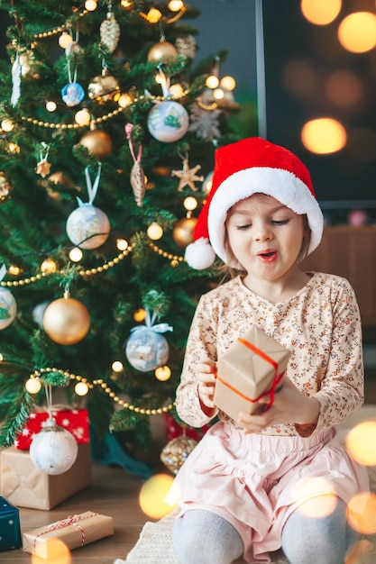 Überraschtes kleines Mädchen mit Geschenkbox nahe dem Weihnachtsbaum